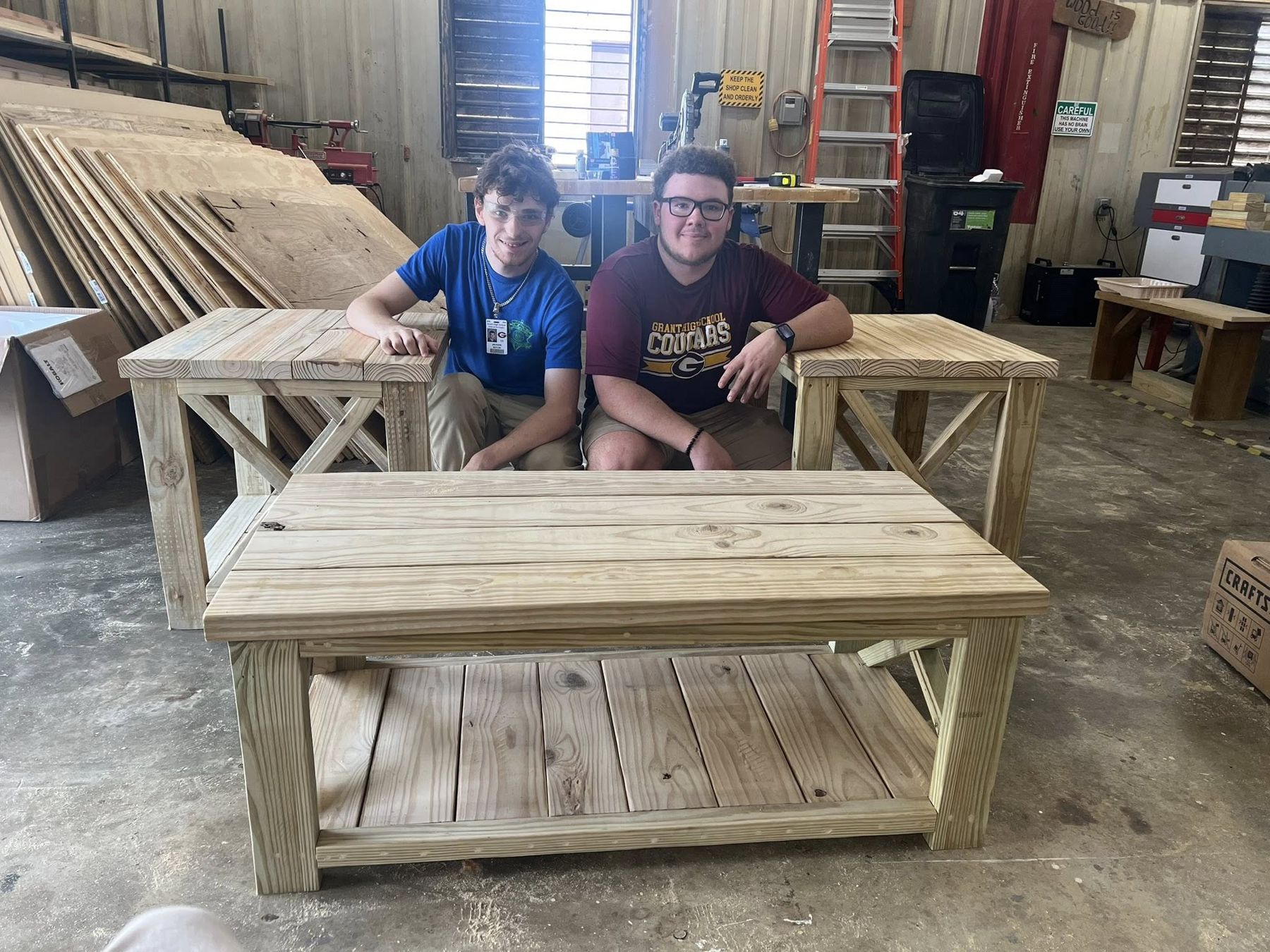 Two students seated at a finished handmade wooden bench and table they built