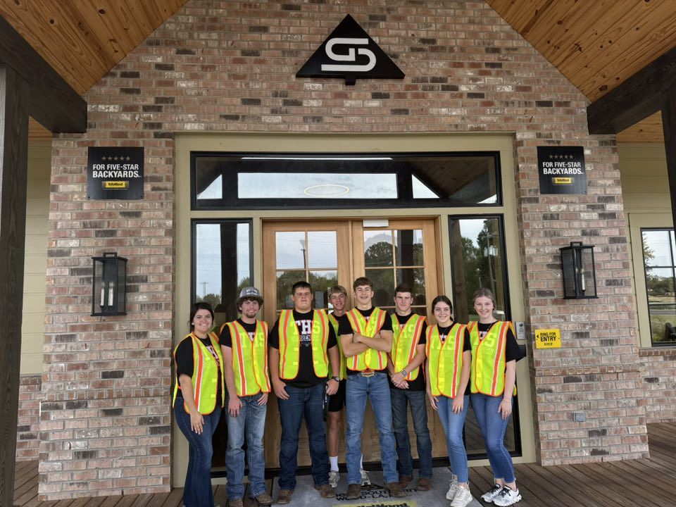 Students in high-visibility vests posing at a job site entrance